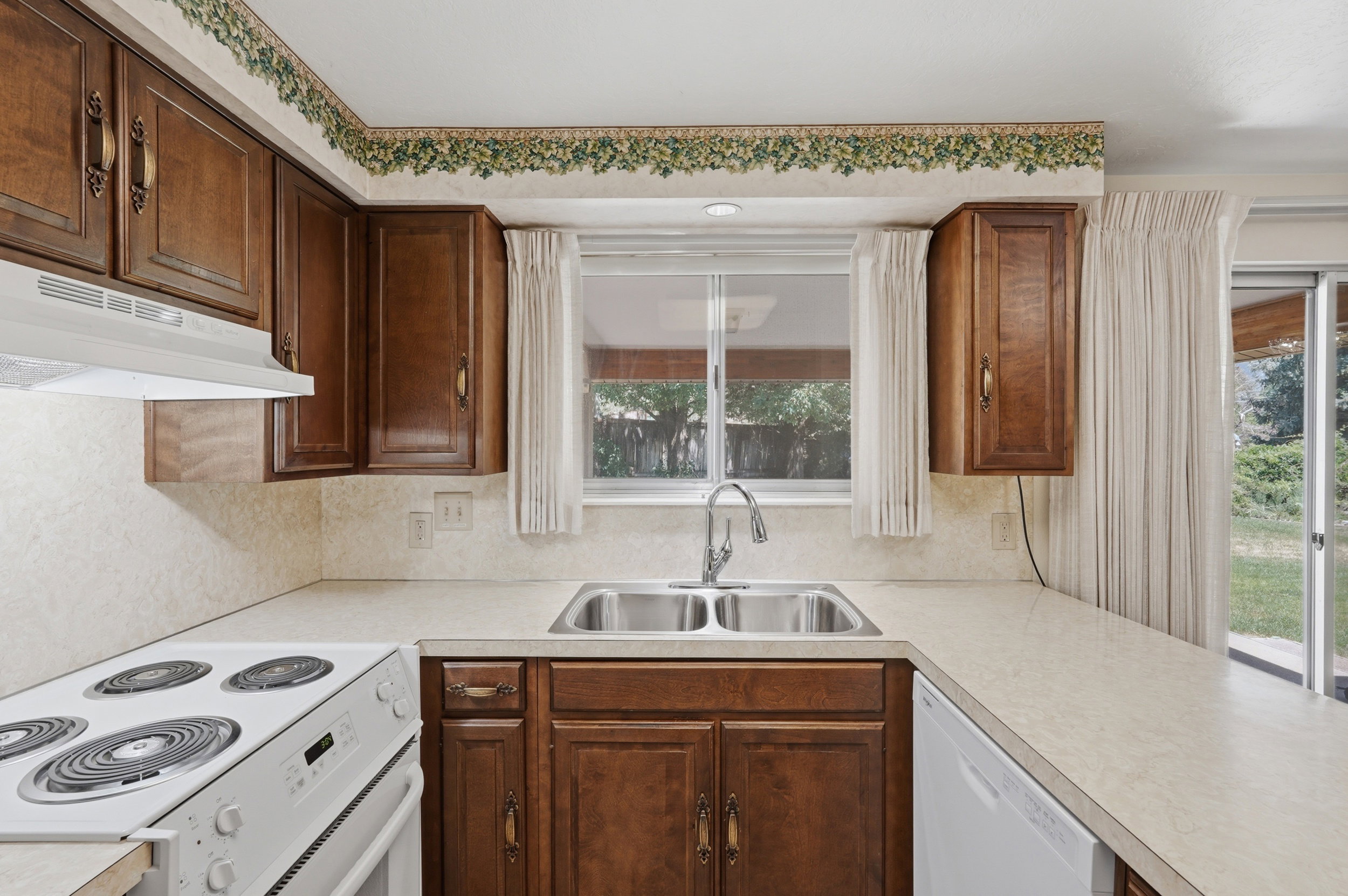 Kitchen featuring wood-finish cabinetry with decorative hardware, a double basin stainless steel sink, and new white electric range and new white dishwasher.