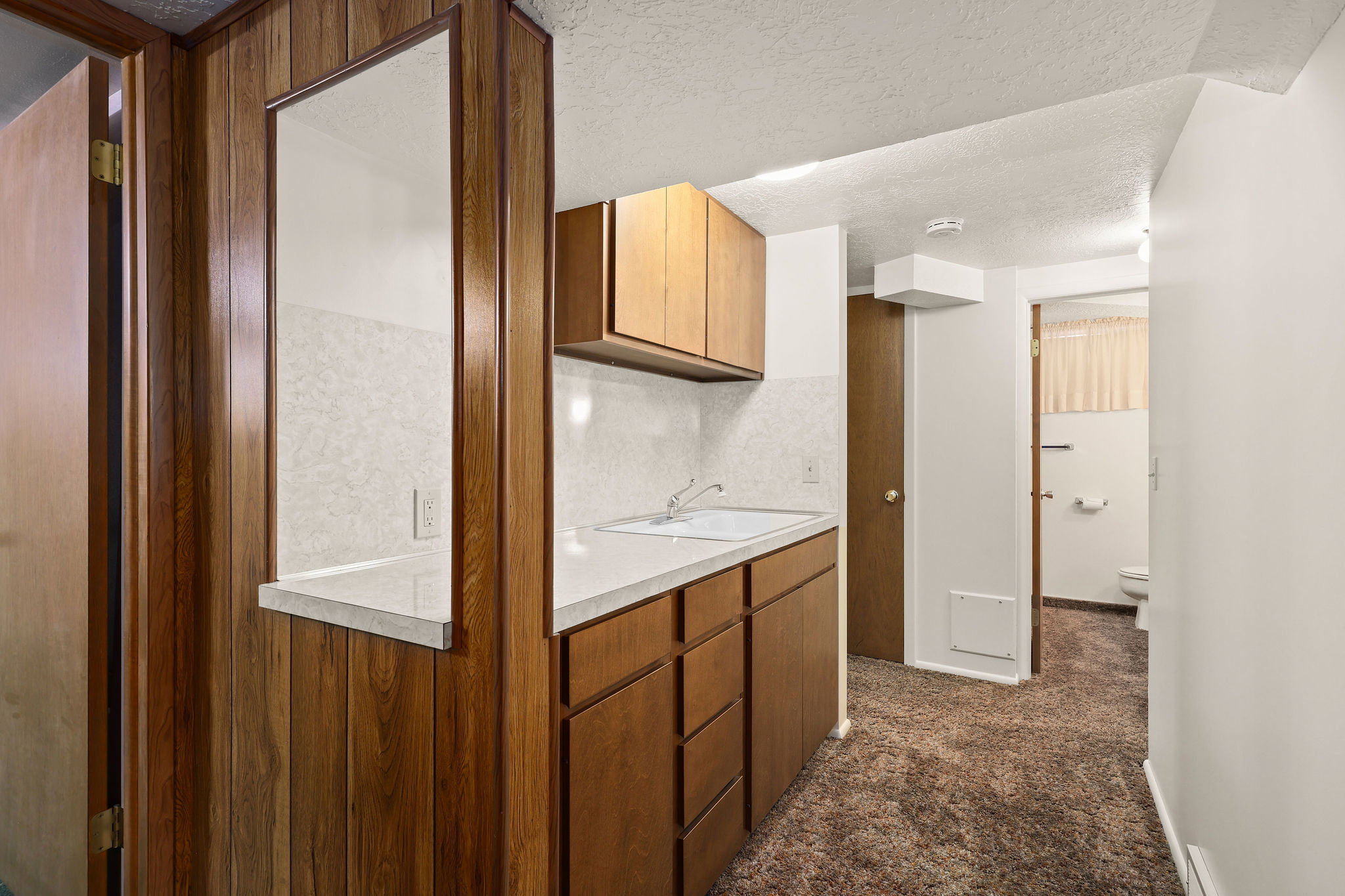 Kitchenette featuring light countertops, a sink, storage, textured ceiling, wood finish cabinets.