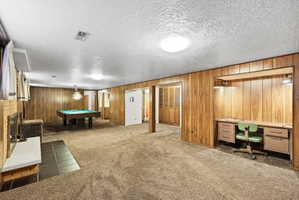 Recreation room featuring a textured ceiling, dark carpet, billiards table, wood walls, and a fireplace