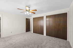 Unfurnished bedroom with multiple closets, carpet flooring, ensuite bath, and ceiling fan