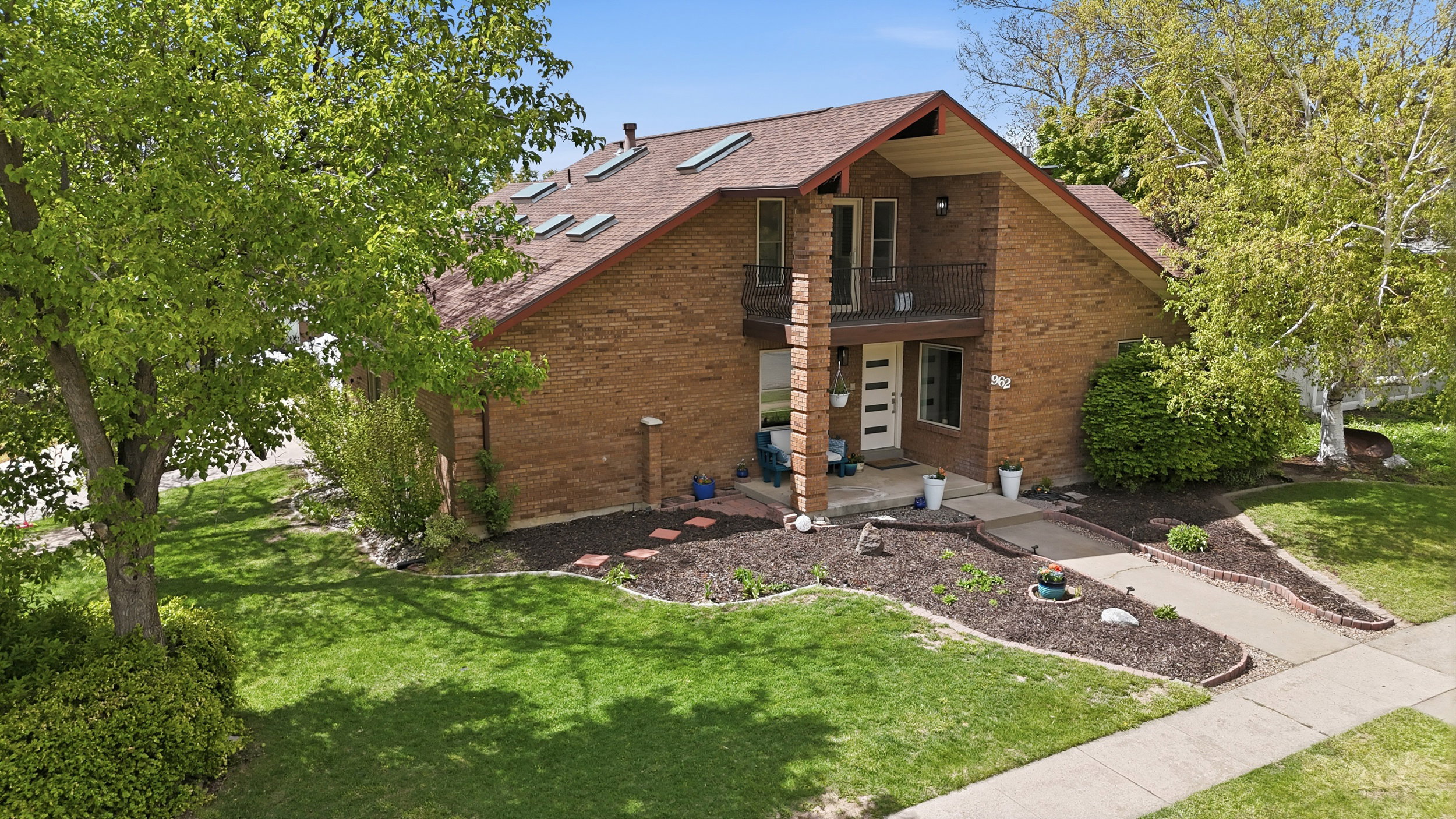 View of front of house featuring a front lawn, a balcony, roof with shingles, and brick siding