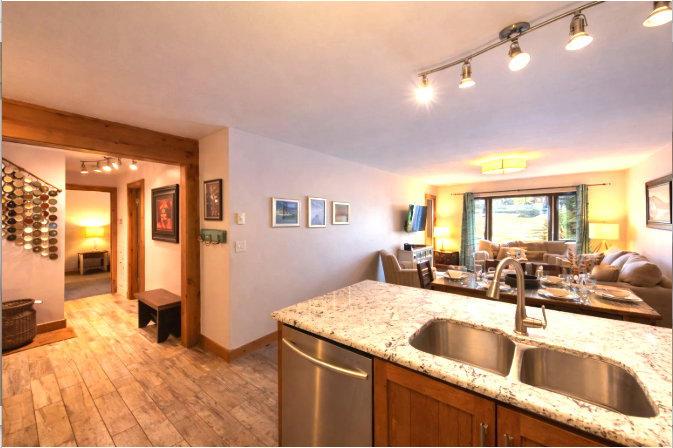 Kitchen featuring rail lighting, open floor plan, dishwasher, light stone counters, and light wood-style floors