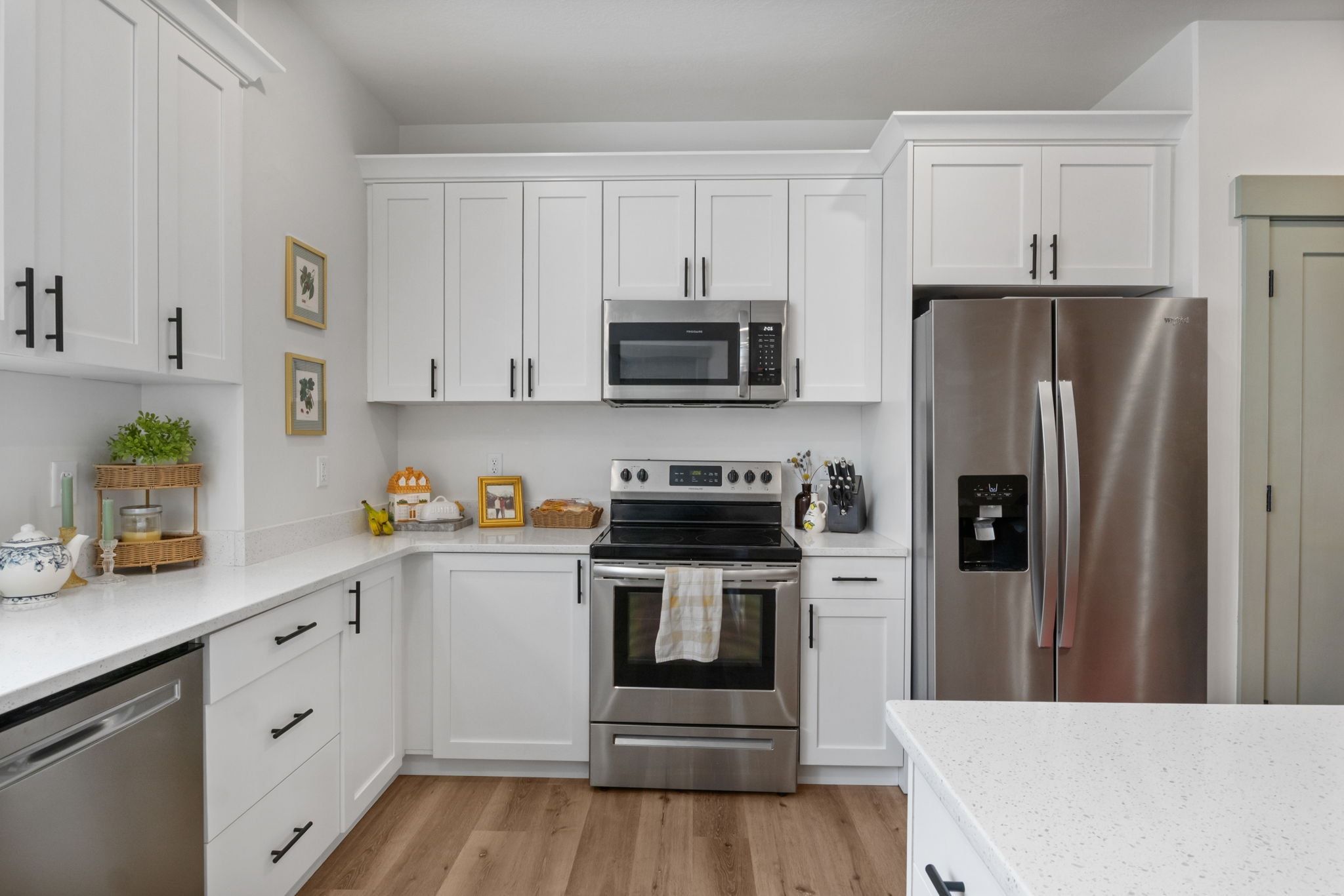 Kitchen featuring stainless steel appliances, white cabinets, light stone counters, and light wood-style floors