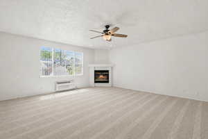 Unfurnished living room featuring light carpet, ceiling fan, a glass covered fireplace, and a textured ceiling