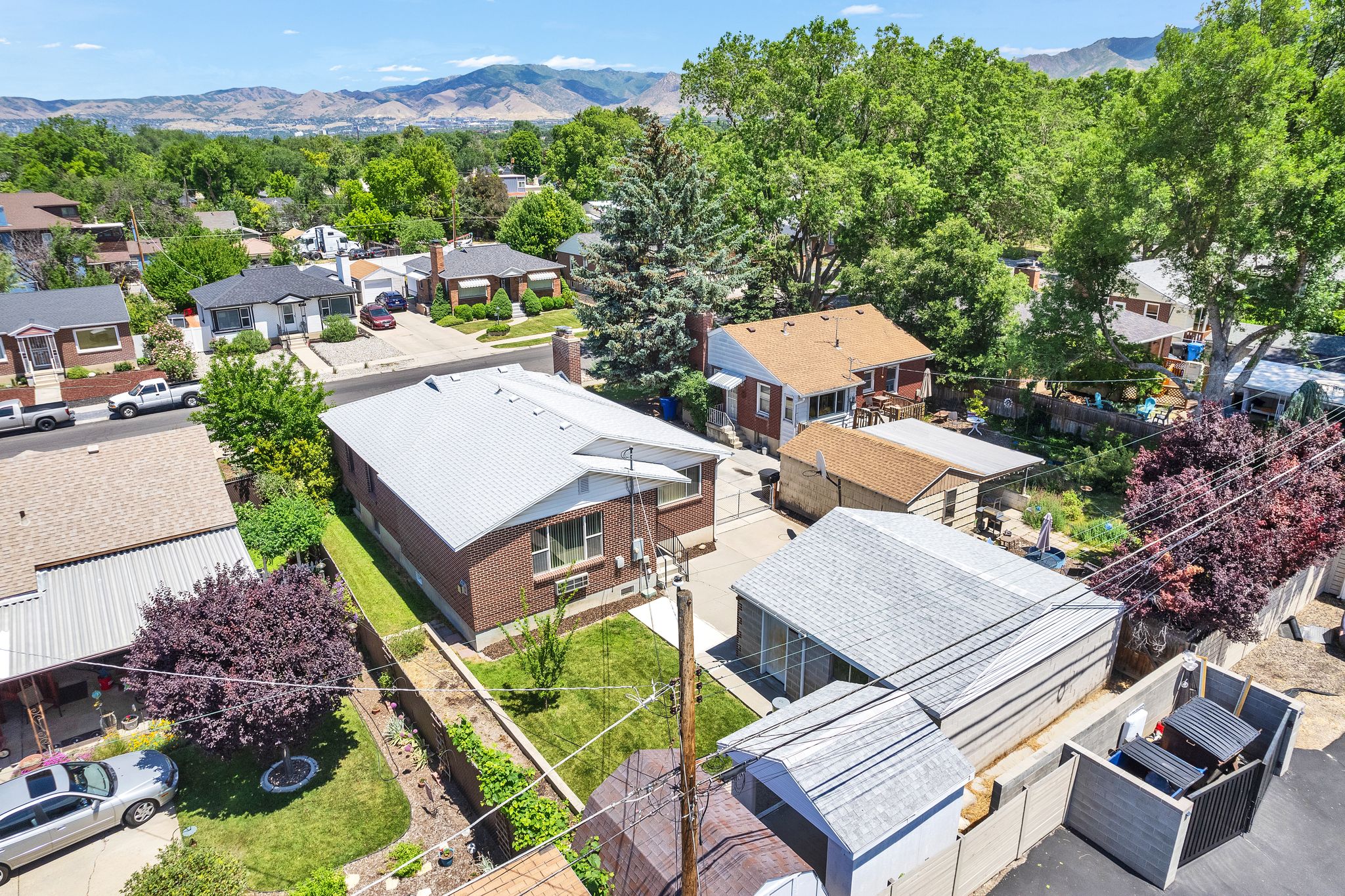 Aerial perspective showcasing a brick residence with a light-colored roof, surrounded by mature trees