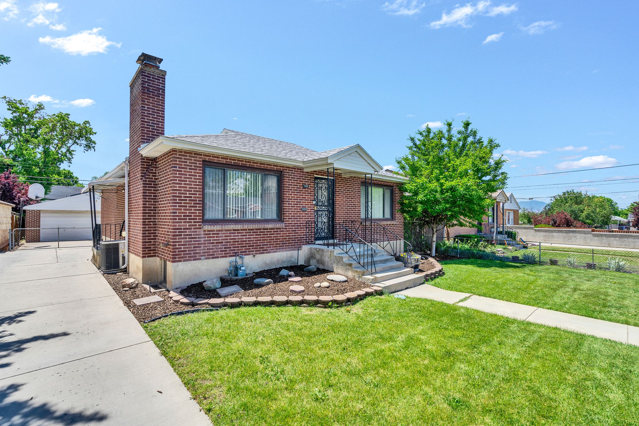 Brick exterior featuring a prominent chimney, concrete driveway, front lawn, and established landscaping