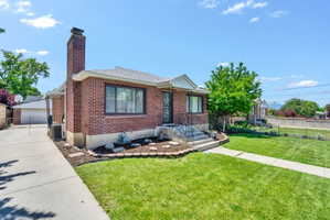 Brick exterior featuring a prominent chimney, concrete driveway, front lawn, and established landscaping