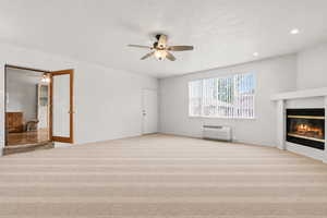 Unfurnished living room featuring a ceiling fan, light colored carpet, a glass covered fireplace, recessed lighting, and a textured ceiling