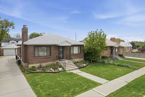 View of front of property featuring a shingled roof, a front yard, a chimney, brick siding, and an outdoor structure