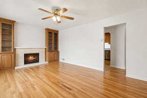 Unfurnished living room with arched walkways, ceiling fan, light wood-style floors, and a high end fireplace