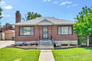 Brick facade residence featuring a front yard with manicured lawn, an ornamental security door, a concrete walkway, and a detached garage structure