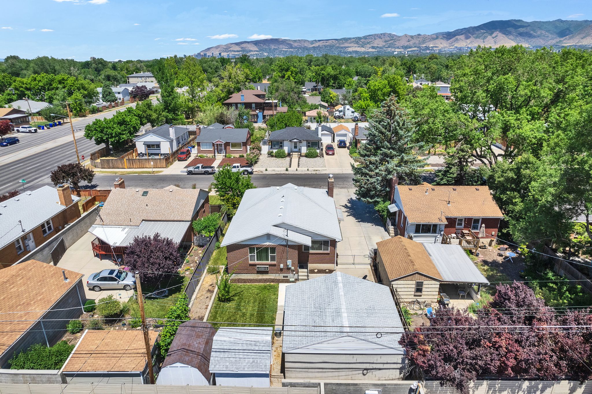 Brick exterior residence with a gray shingle roof, established landscaping, a paved driveway, and a fenced backyard