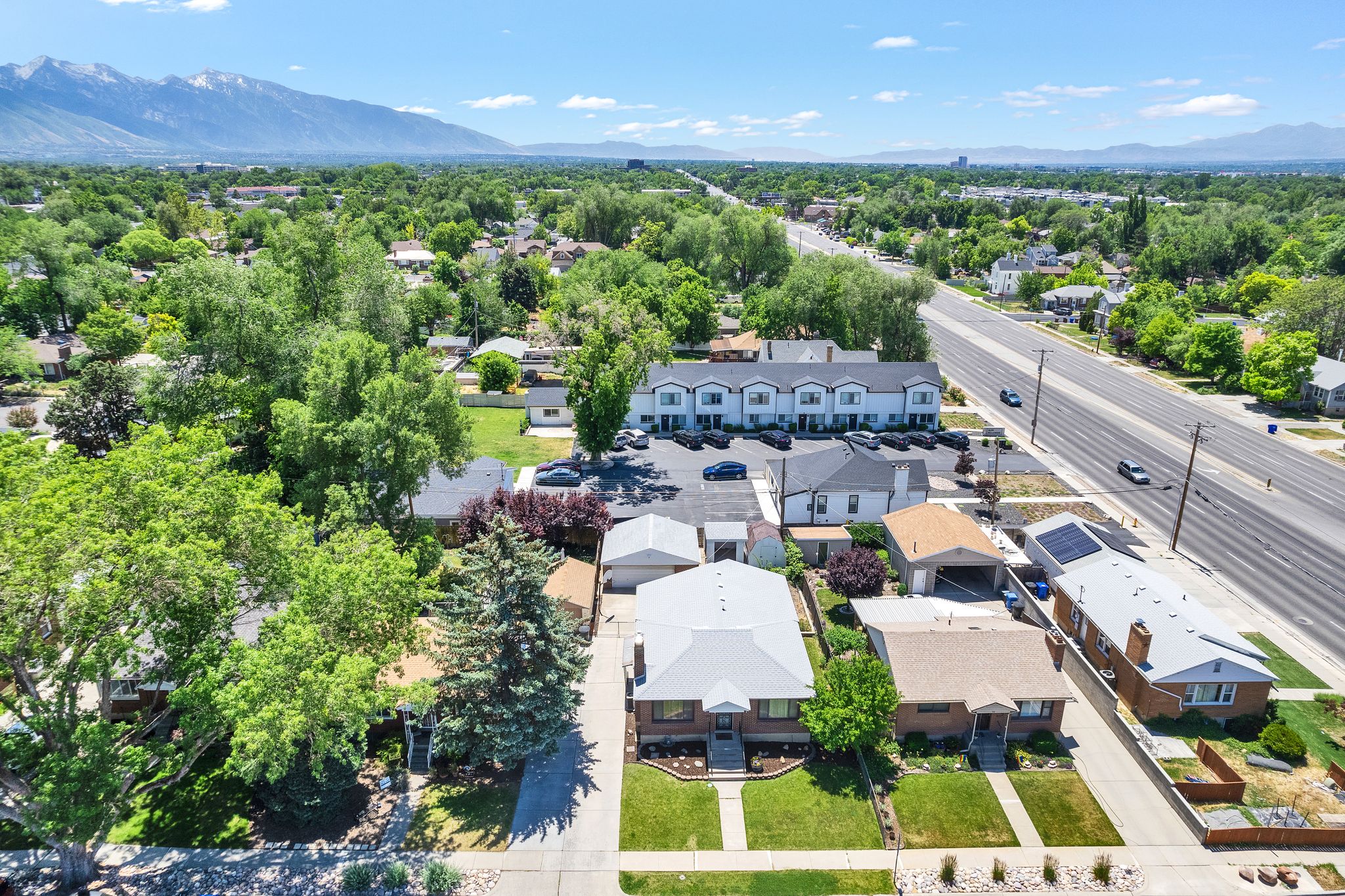 Aerial perspective showcasing residential properties with mature trees, a multi-lane road, and distant mountains
