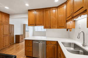 Kitchen featuring wood finish cabinetry, dishwasher, light wood-style floors, recessed lighting, and light stone counters