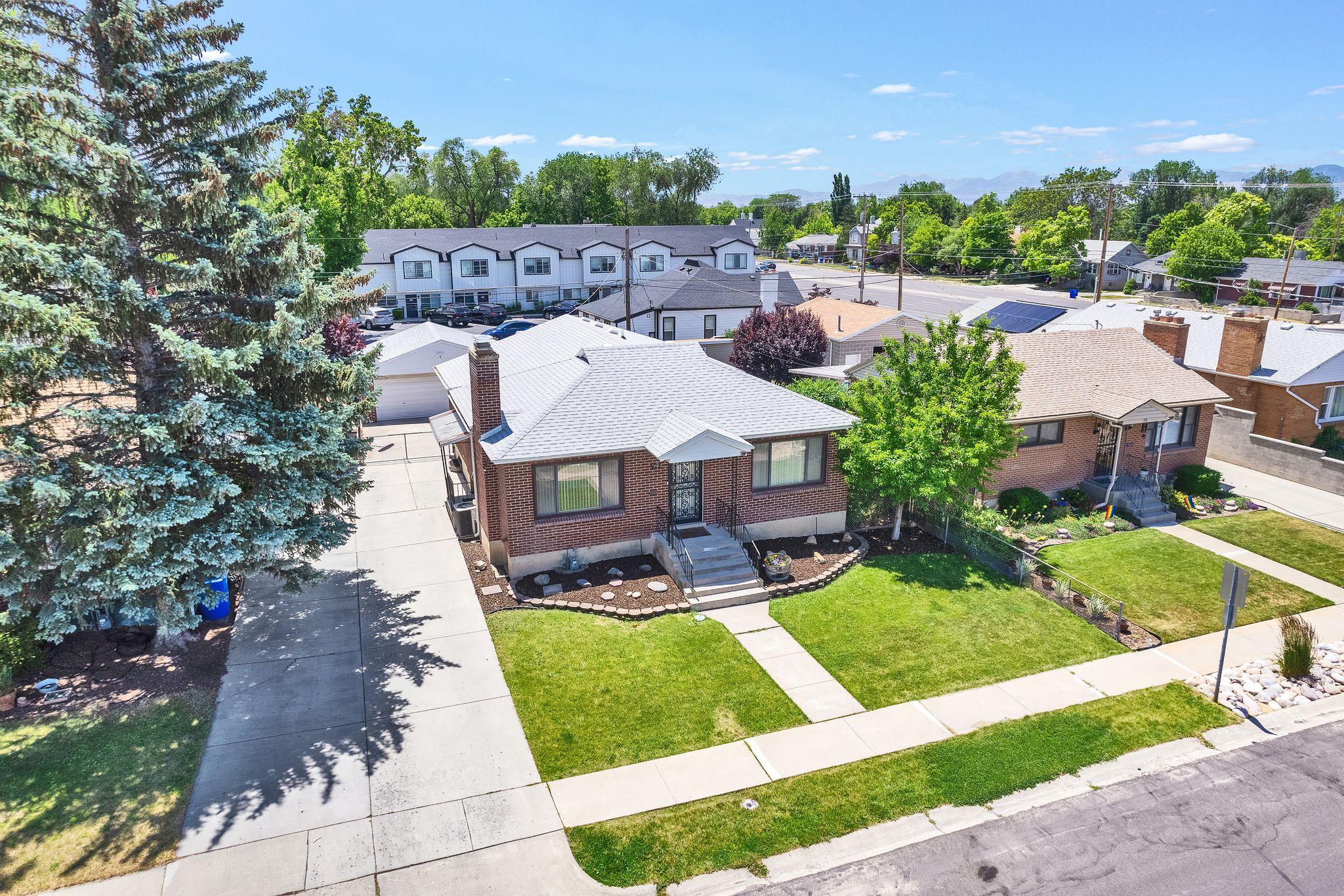 Brick exterior residence with a gray shingle roof, featuring a concrete driveway, a manicured front lawn, and foundational landscaping