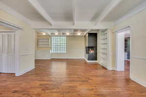 Unfurnished living room featuring built in features, wood finished floors, a brick fireplace, and beam ceiling