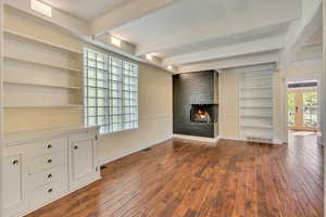 Unfurnished living room with built in shelves, a fireplace, beamed ceiling, and dark wood-style flooring