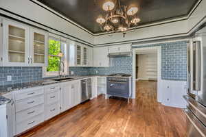 Kitchen featuring white cabinets, glass fronted cabinets, dark wood-style flooring, dark stone counters, and decorative backsplash