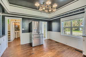 Kitchen with suspended lighting, stainless steel fridge, wainscoting, dark wood-type flooring, and healthy amount of natural light