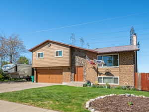 Bi-level home featuring brick siding, an attached garage, driveway, a chimney, and a standing seam roof