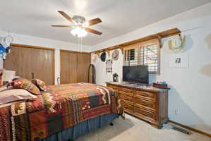 Bedroom featuring two closets, light colored carpet, and ceiling fan