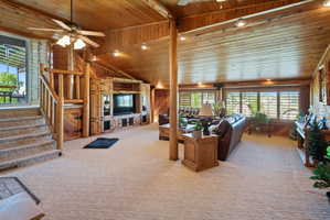 Living room with a ceiling fan, wooden walls, healthy amount of natural light, light colored carpet, and wood ceiling