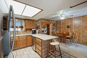 Kitchen featuring stainless steel appliances, a peninsula, light countertops, wood finish cabinets, and a breakfast bar