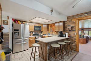 Kitchen featuring brick wall, a breakfast bar, light countertops, stainless steel appliances, and a peninsula