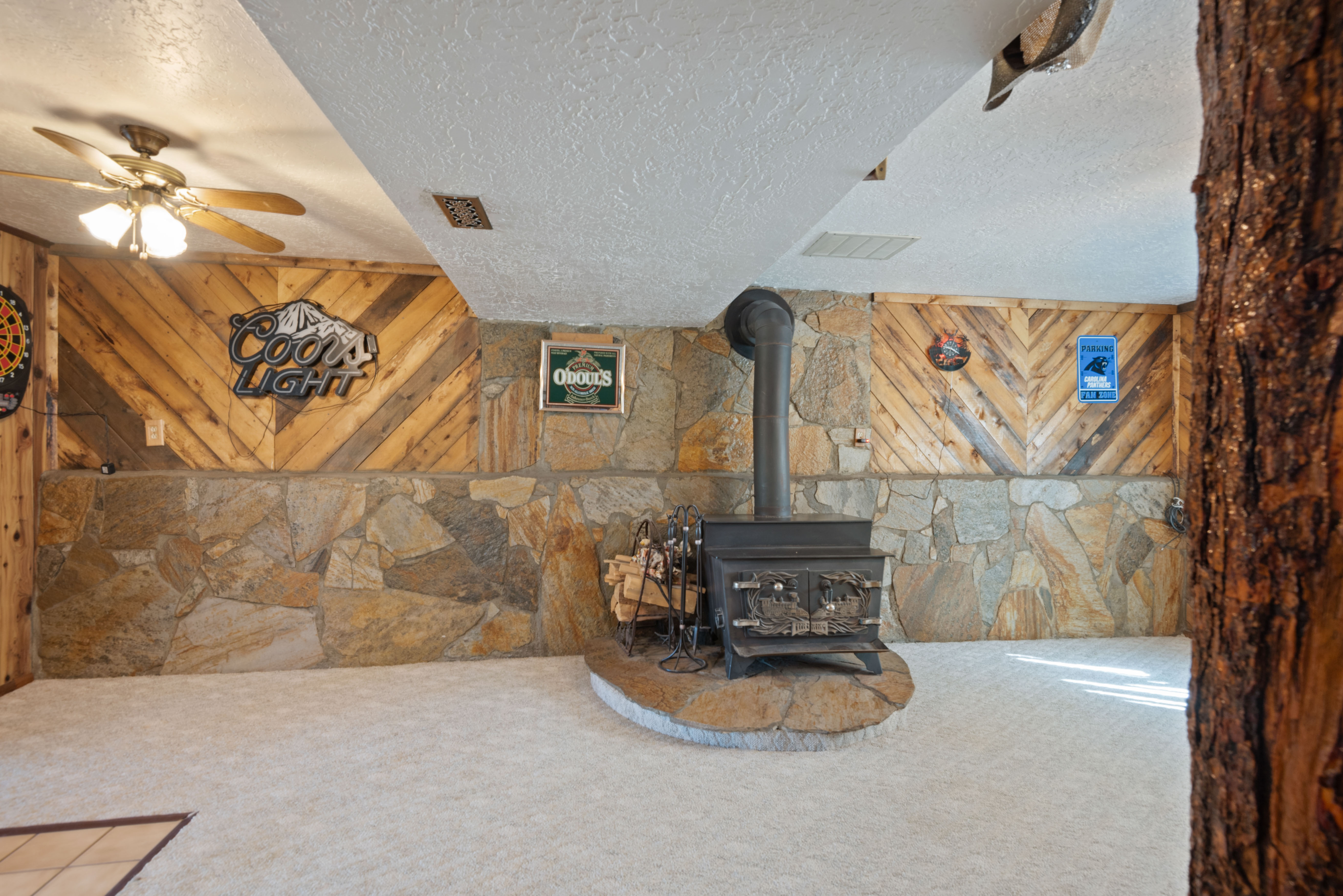 Unfurnished living room featuring a textured ceiling, a wood stove, carpet floors, ceiling fan, and wood walls