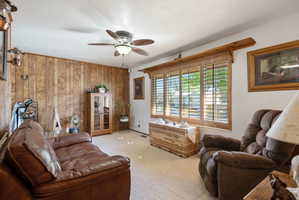 Living area with wooden walls, light colored carpet, ceiling fan, and a textured ceiling