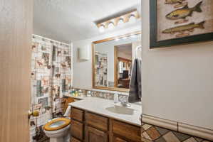 Full bath featuring a shower with shower curtain, vanity, a textured ceiling, and decorative backsplash