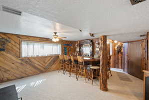 Carpeted dining area with wooden walls, ceiling fan, and a textured ceiling