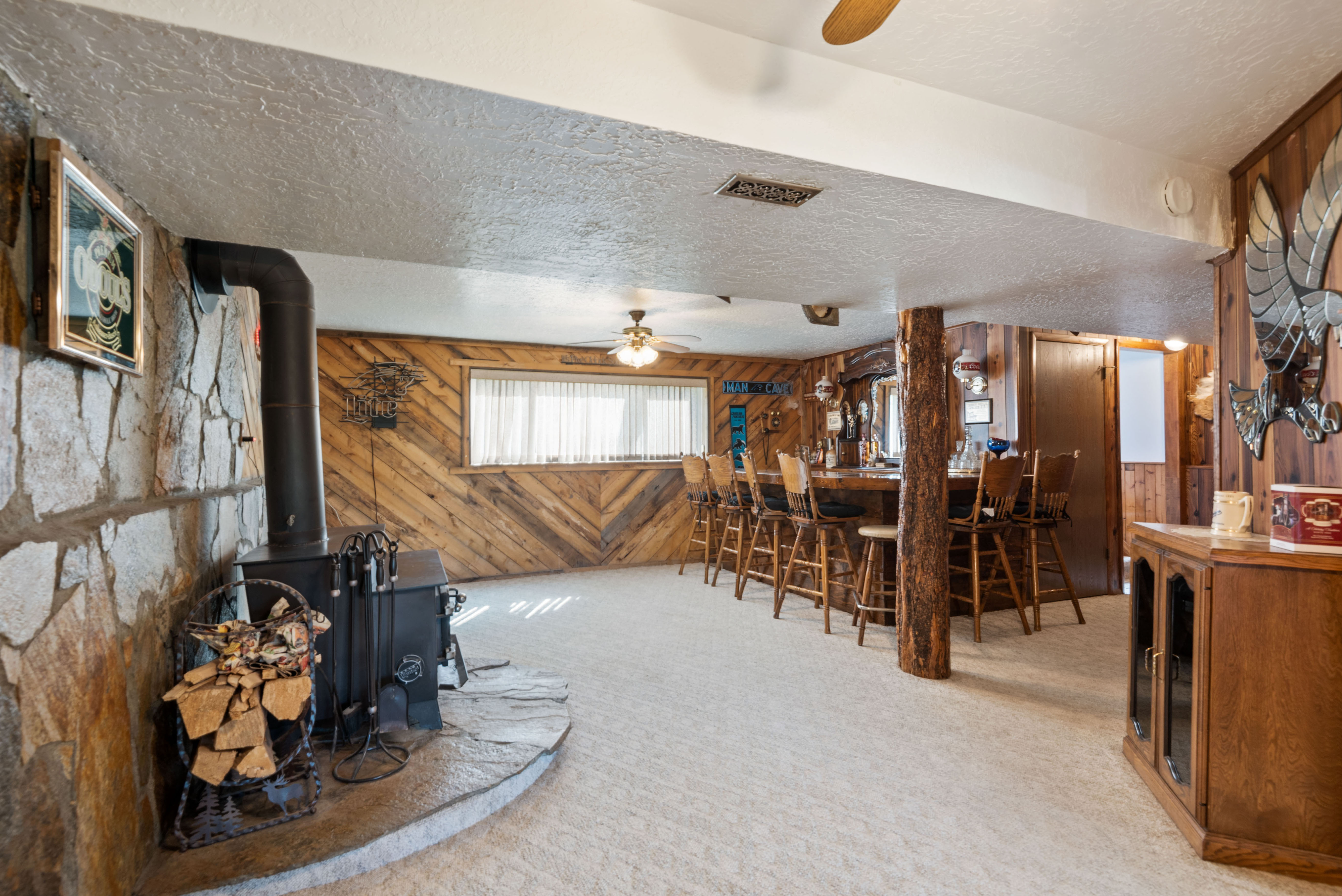 Dining space with a ceiling fan, wooden walls, light carpet, a textured ceiling, and a wood stove