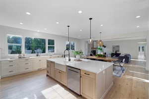 Kitchen featuring open floor plan, a center island with sink, light wood-type flooring, stainless steel dishwasher, and light stone countertops