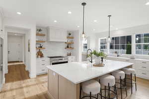 Two tone kitchen featuring an island with sink, decorative light fixtures, light wood finished floors, open shelves, and a breakfast bar