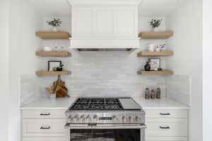 Kitchen with white cabinetry, open shelves, high end stainless steel range oven, and decorative backsplash