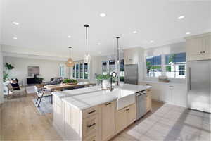 Kitchen with stainless steel appliances, open floor plan, a center island with sink, light wood finished floors, and hanging light fixtures