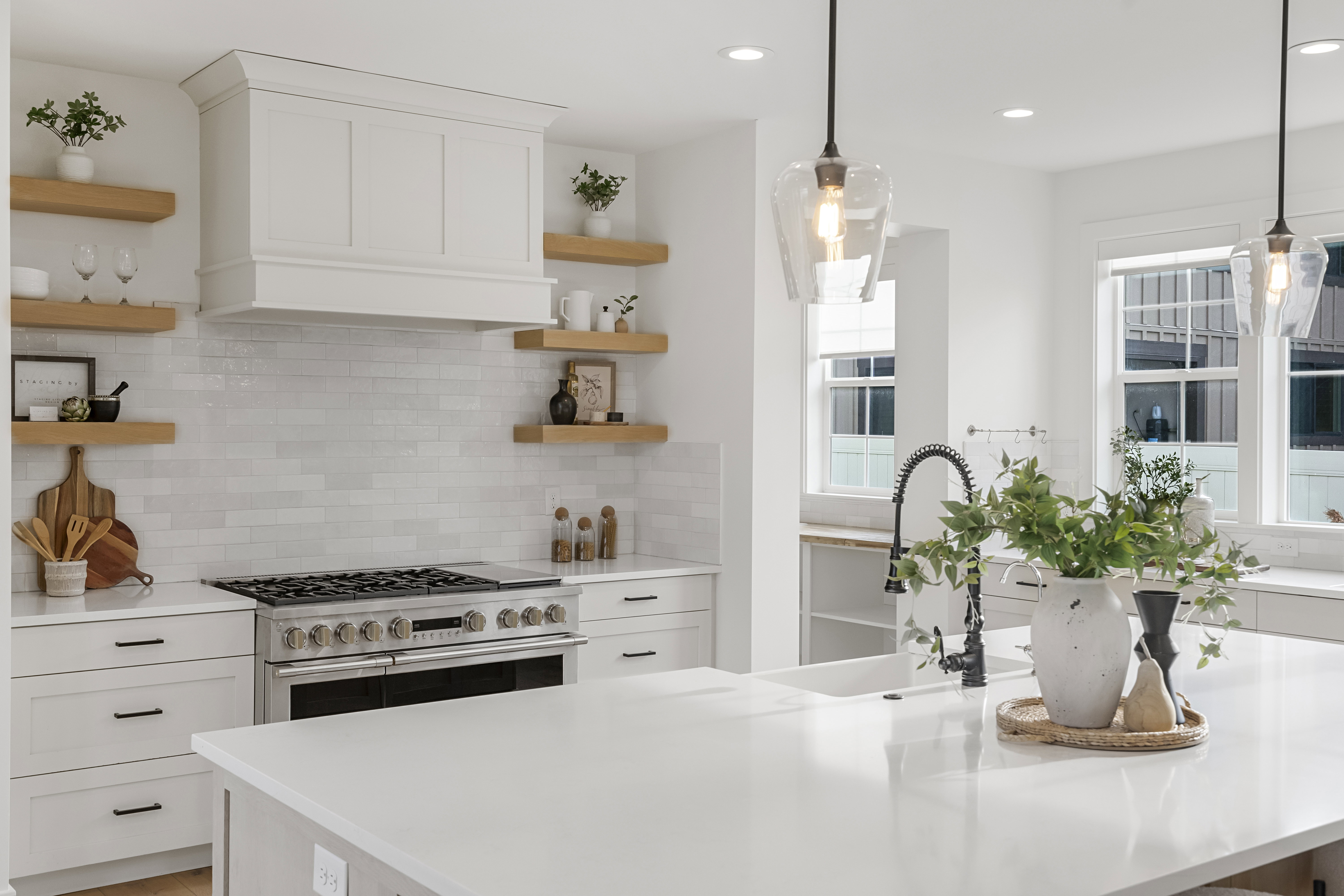 Kitchen with open shelves, white cabinets, range with two ovens, and light stone counters