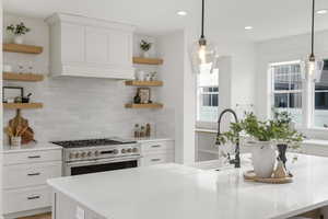 Kitchen with open shelves, white cabinets, range with two ovens, and light stone counters
