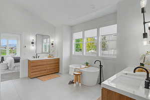 Ensuite bathroom featuring vanity, a freestanding bath, lofted ceiling, and light tile patterned floors