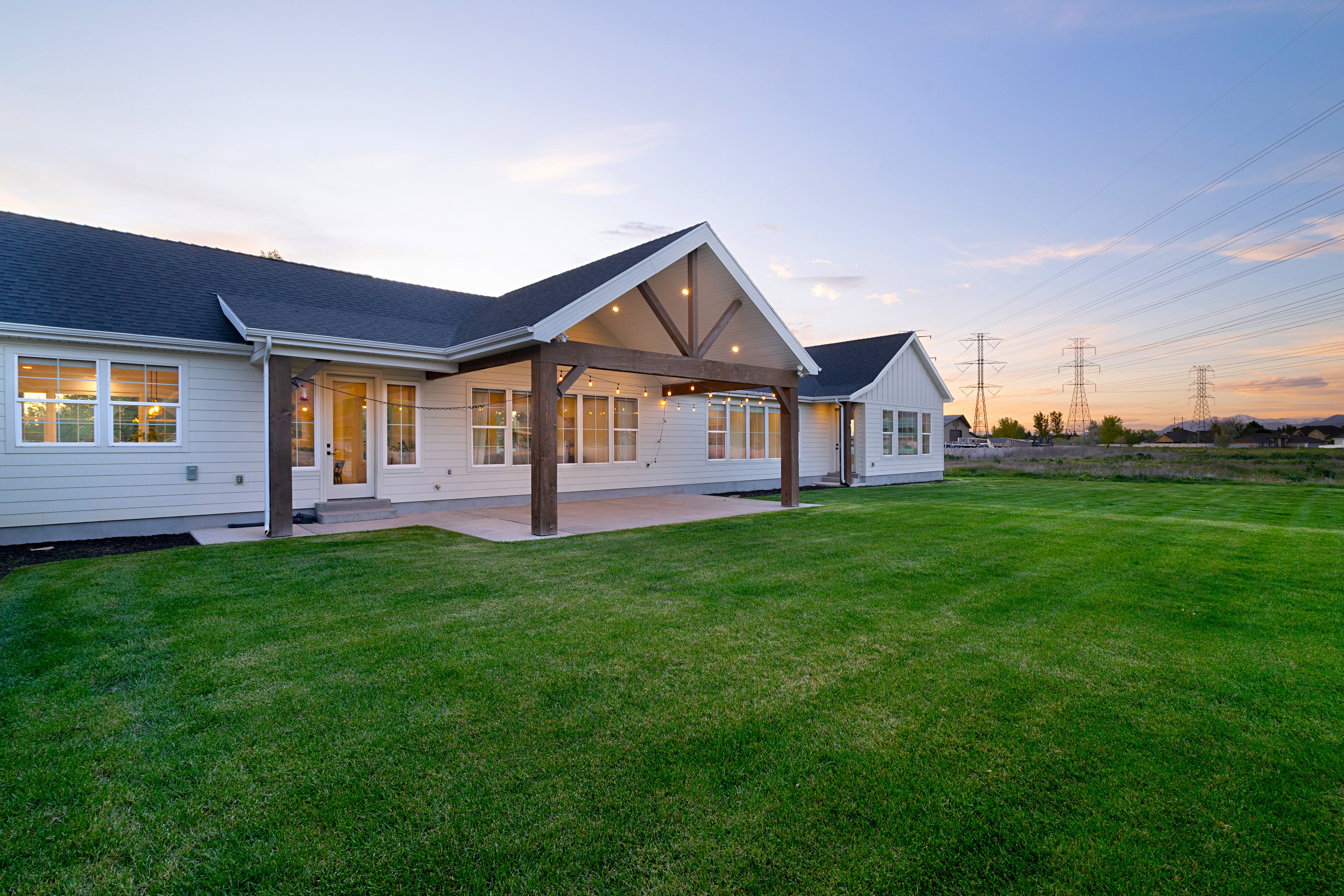 Back of property at dusk featuring a patio area, a lawn, and a shingled roof