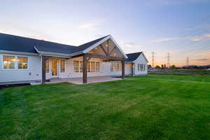 Back of property at dusk featuring a patio area, a lawn, and a shingled roof