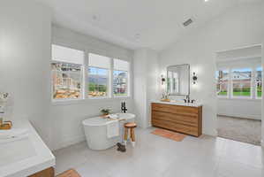 Bathroom featuring double vanity, lofted ceiling, a freestanding tub, recessed lighting, and light tile patterned floors