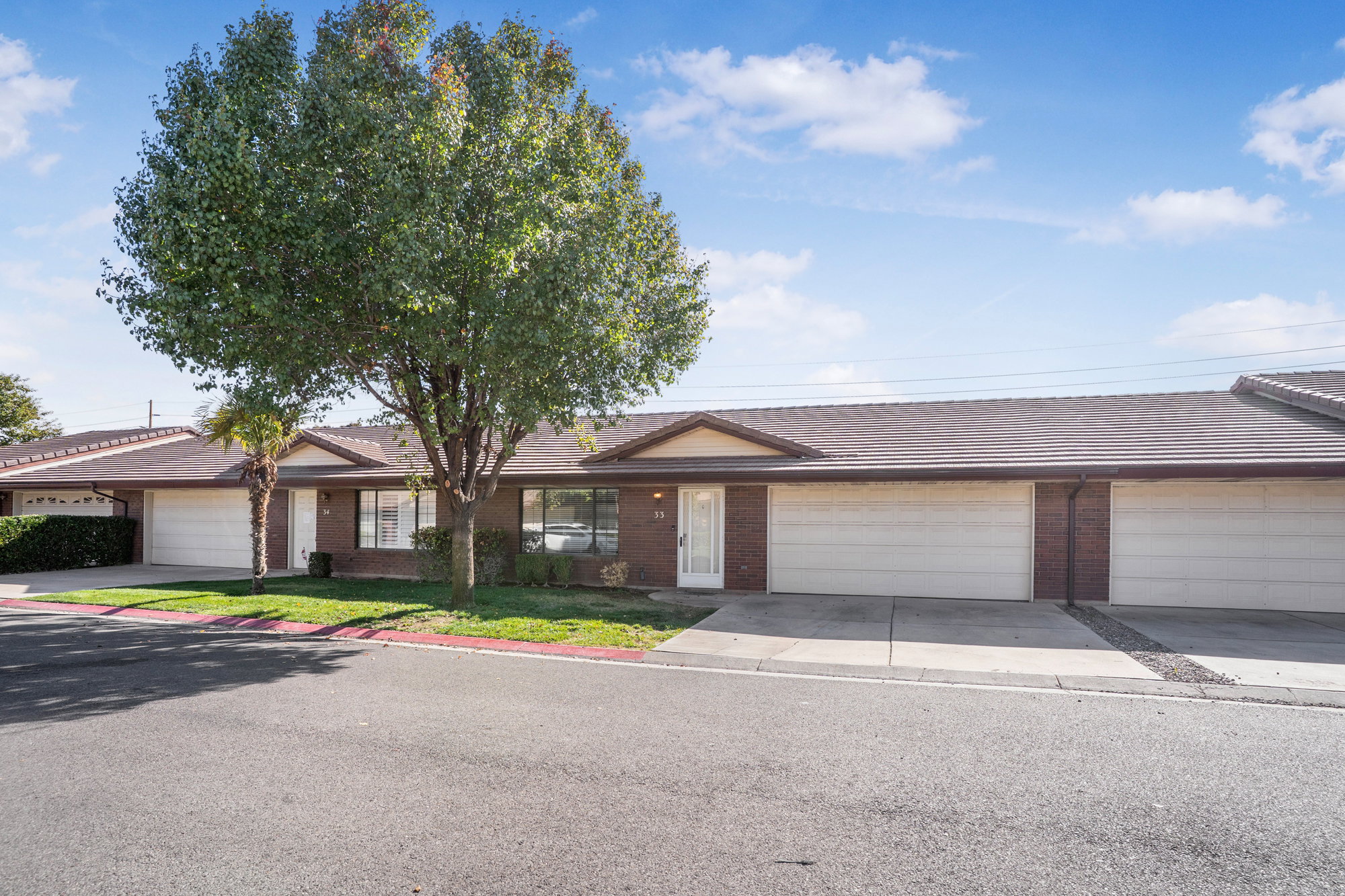 Ranch-style home featuring brick siding, driveway, a tile roof, a garage, and a front lawn