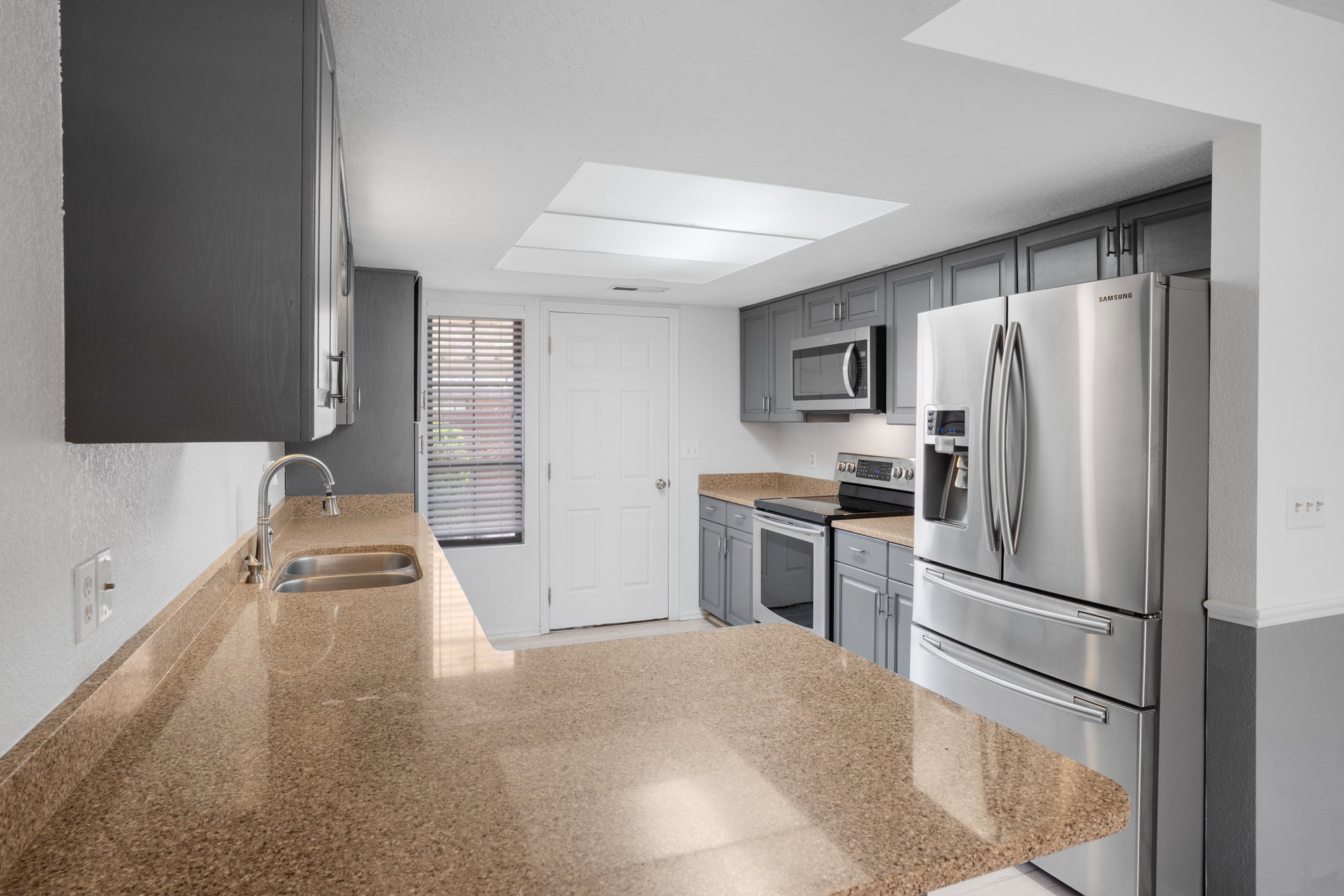 Kitchen featuring stainless steel appliances, gray cabinetry, light stone counters, a peninsula, and a textured wall