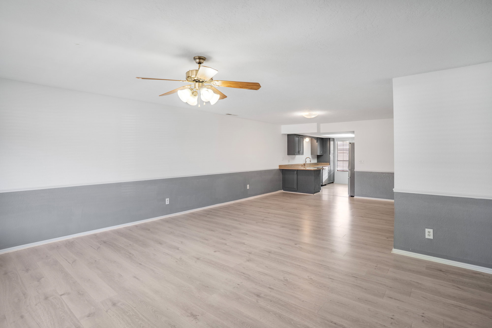 Unfurnished living room with ceiling fan, light wood-type flooring, and wainscoting