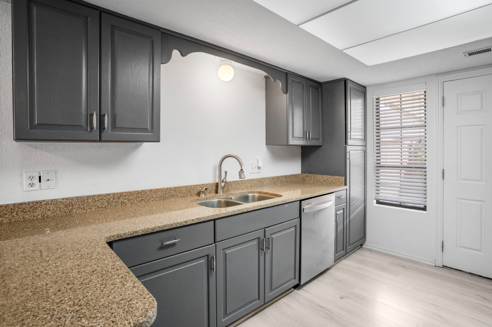 Kitchen featuring gray cabinets, light stone counters, light wood-type flooring, and stainless steel dishwasher