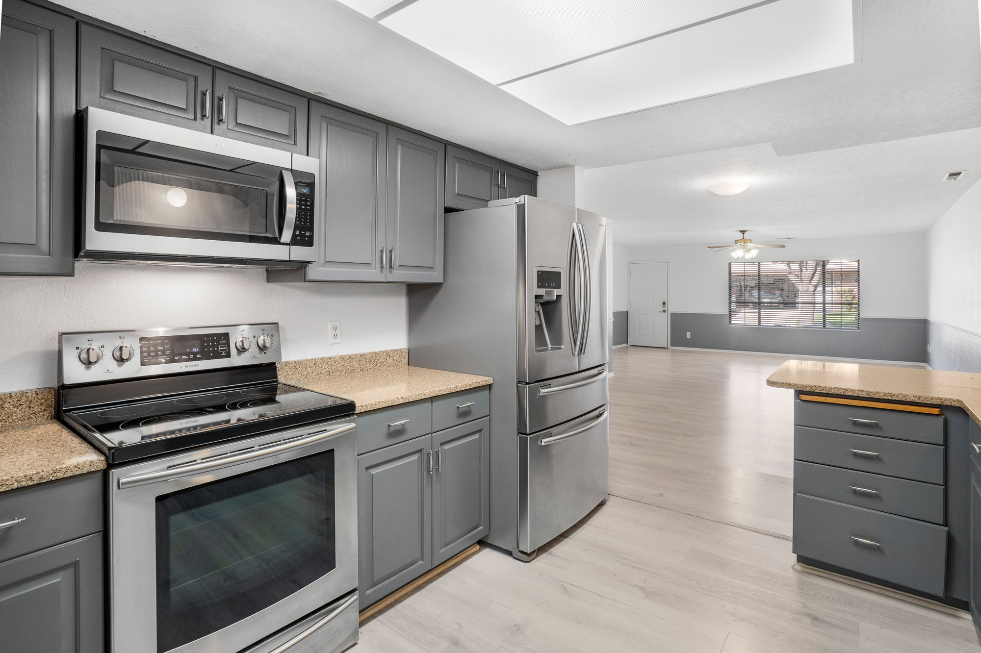 Kitchen featuring gray cabinets, stainless steel appliances, light wood-type flooring, light stone counters, and a wainscoted wall