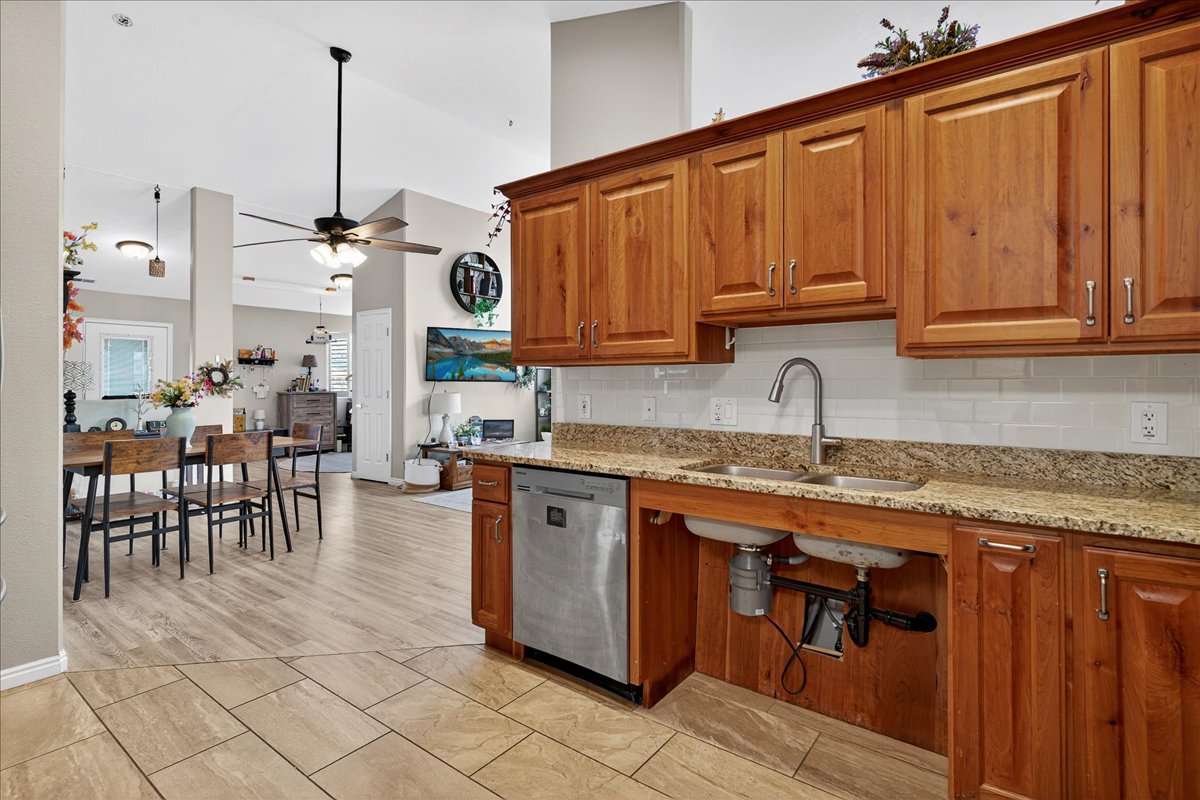 Kitchen featuring wood finish cabinets, light stone counters, a ceiling fan, decorative backsplash, and lofted ceiling