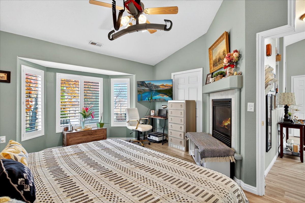 Bedroom featuring wood finished floors, vaulted ceiling, a glass covered fireplace, and a ceiling fan